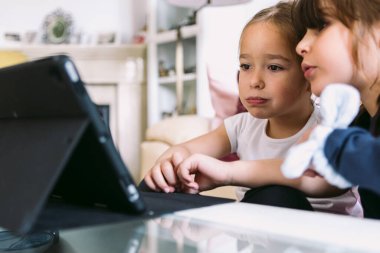 İki küçük kız dikkatle oturma odalarındaki tablette bir video izliyorlar. Çocukluk kavramı, teknoloji, öğrenme, eğlenme, internet ve bağlantı.