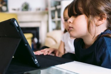 İki küçük kız dikkatle oturma odalarındaki tablette bir video izliyorlar. Çocukluk kavramı, teknoloji, öğrenme, eğlenme, internet ve bağlantı.