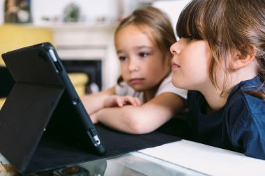 İki küçük kız dikkatle oturma odalarındaki tablette bir video izliyorlar. Çocukluk kavramı, teknoloji, öğrenme, eğlenme, internet ve bağlantı.