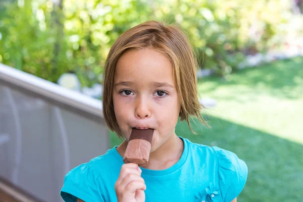Girl wearing a green t-shirt, having a milk chocolate ice cream, in the street, in summer. Ice cream, popsicle, eating, sweet and summer concept.