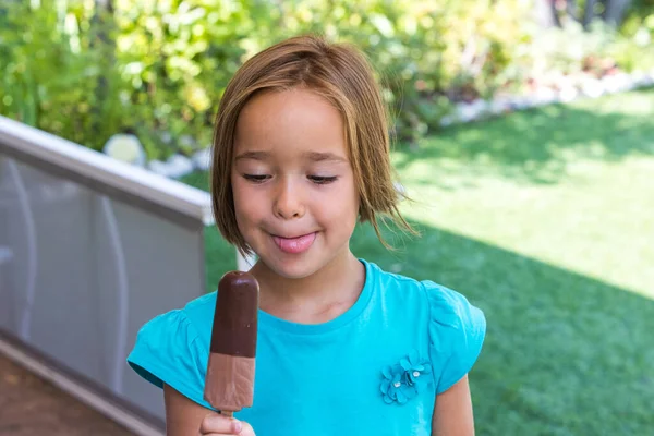 Girl wearing green t-shirt, holding a milk chocolate ice cream, in the street, in summer, looking at the ice cream. Ice cream, popsicle, eating, sweet and summer concept.