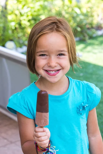 Girl wearing green t-shirt, holding a milk chocolate ice cream, in the street, in summer, smiling. Ice cream, popsicle, eating, sweet and summer concept.
