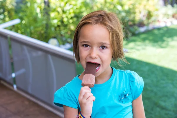 Girl wearing a green t-shirt, having a milk chocolate ice cream, in the street, in summer. Ice cream, popsicle, eating, sweet and summer concept.