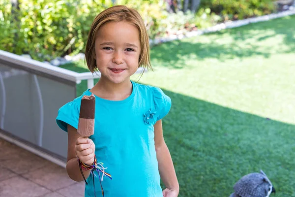 Unknown girl, wearing a green t-shirt, holding a milk chocolate ice cream, on the street, in summer, looking at the camera. Ice cream, popsicle, eating, sweet and summer concept.