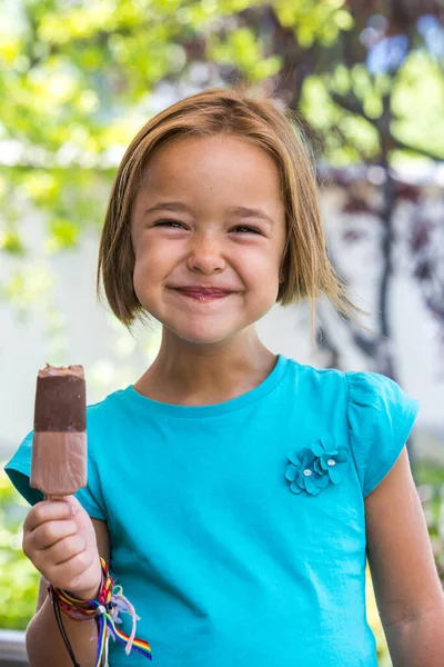 Unknown girl, wearing a green t-shirt, holding a milk chocolate ice cream, on the street, in summer, looking at the camera. Ice cream, popsicle, eating, sweet and summer concept.