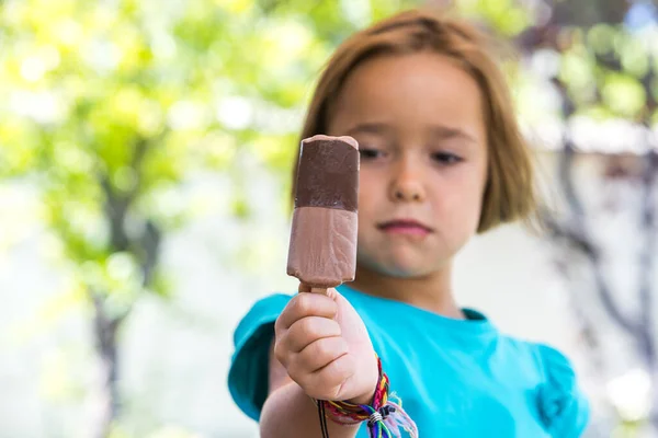 Unknown girl, wearing green shirt. out of focus, holding a milk chocolate ice cream, focused, on the street, in summer. Ice cream, popsicle, eating, sweet and summer concept.