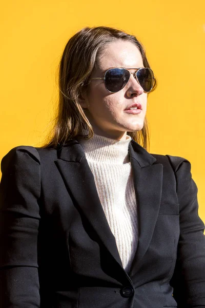 Executive entrepreneur woman, wearing black jacket and wool sweater and sunglasses, on yellow background in the street, with copy space. Entrepreneur woman concept.