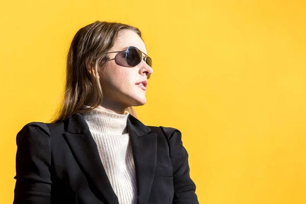 Executive entrepreneur woman, wearing black jacket and wool sweater and sunglasses, on yellow background in the street, with copy space. Entrepreneur woman concept.