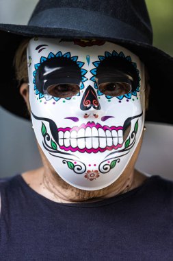 Catrina maskeli ve şapkalı yaşlı bir kadının portresi Cadılar Bayramı 'nı ve Ruhlar Günü' nü sokakta kutluyor. Kutlama, kostüm, parti ve maske konsepti.