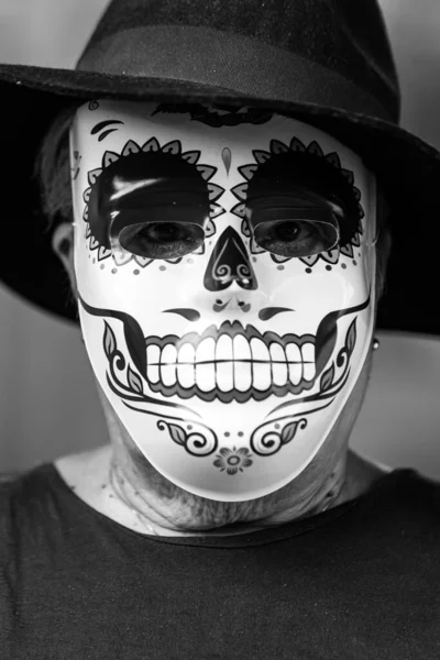 Black and white portrait of an elderly lady with a catrina mask and hat, celebrating Halloween and All Souls\' Day, on a white background. Celebration, costume, party and mask concept.