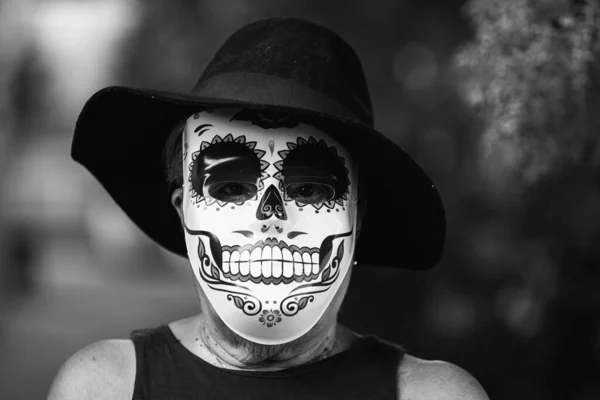 Black and white portrait of an elderly lady with a catrina mask and hat, celebrating Halloween and All Souls\' Day, on the street. Celebration, costume, party and mask concept.
