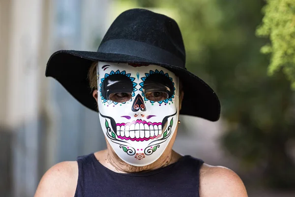 Portrait of an elderly lady with a catrina mask and hat, celebrating Halloween and All Souls\' Day, on the street. Celebration, costume, party and mask concept.