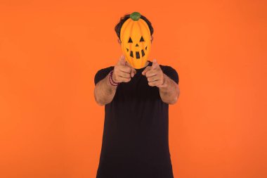 Cadılar Bayramı 'nı kutlayan, turuncu arka planda kameraya bakan balkabağı maskeli kişi. Kutlama kavramı, Ruhlar Günü ve Azizler Günü..