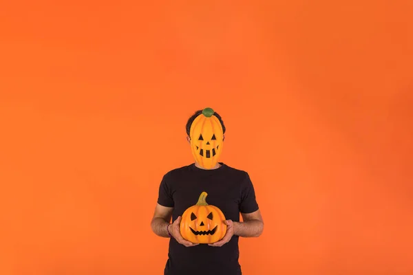 Person with pumpkin mask celebrating Halloween, holding a pumpkin, on orange background. Concept of celebration, All Souls\' Day and All Saints\' Day.