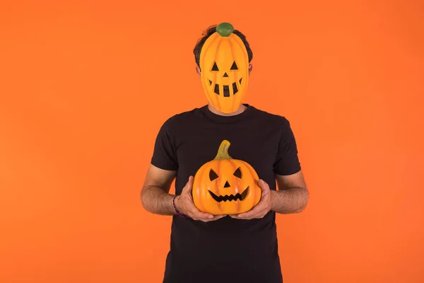 Person with pumpkin mask celebrating Halloween, holding a pumpkin, on orange background. Concept of celebration, All Souls\' Day and All Saints\' Day.