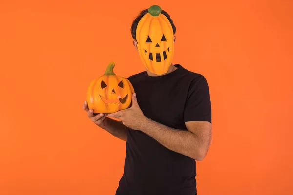 Person with pumpkin mask celebrating Halloween, holding a pumpkin, on orange background. Concept of celebration, All Souls' Day and All Saints' Day.