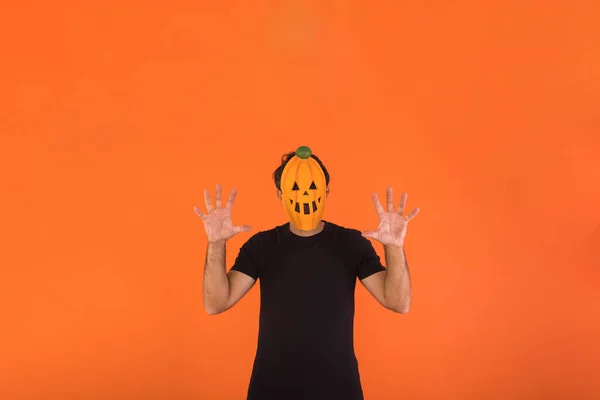 Person with pumpkin mask celebrating Halloween, scaring, on orange background. Concept of celebration, All Souls\' Day and All Saints\' Day.