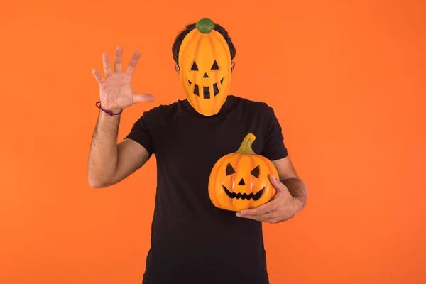 Person with pumpkin mask celebrating Halloween, scaring and holding a pumpkin, on orange background. Concept of celebration, All Souls\' Day and All Saints\' Day.