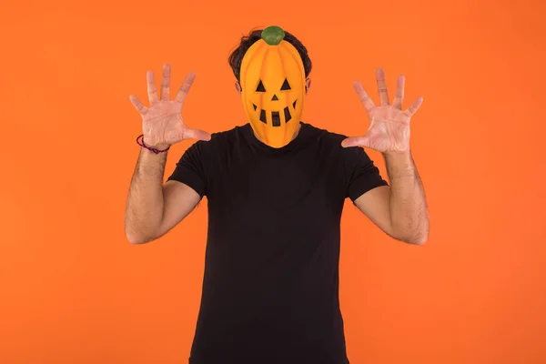 Person with pumpkin mask celebrating Halloween, scaring, on orange background. Concept of celebration, All Souls\' Day and All Saints\' Day.