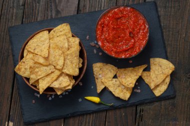 Mexican corn chips nachos with salsa dip. Crispy nachos with spicy red sauce, top view.