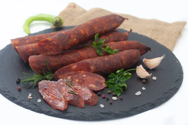 新鮮なハーブやスパイスと黒ボード上の豚肉の肉で作られた乾燥ソーセージ 白地に自家製ソーセージの燻製 — ストック写真