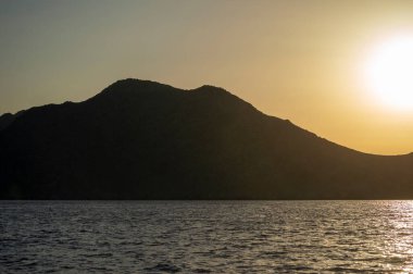 Ege Denizi 'ndeki Yunan adaları üzerinde batmış bir deniz manzarası. Tepelerin silueti