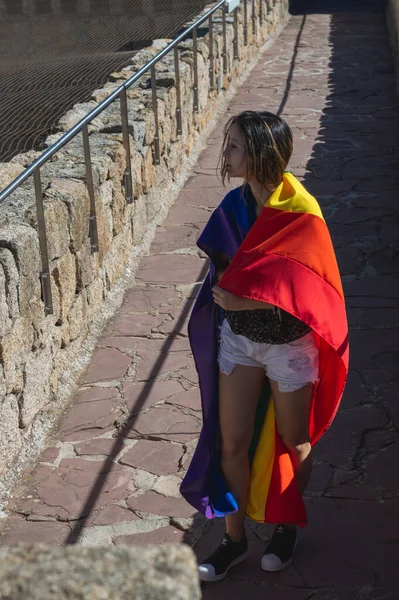 Portrait of an attractive woman holding a rainbow flag on her shoulders, looking to the side. Gay pride concept. Freedom.