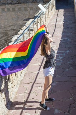 Young woman holding and raising a rainbow flag with closed eyes