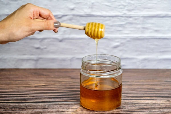 Bal çiseleme. Bal çömleği ve tahta sopa izole edilmiş beyaz tuğla duvar