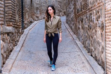 Ortaçağ şehrinin dar sokaklarında yeşil asker gömleği giyen genç bir gezgin.