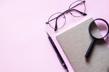 Siyah defter düzeninde gözlük ve büyüteç. Metin için boş bırak. Pastel pembe arka planda