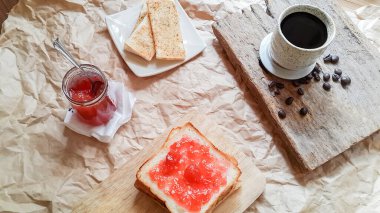 Üst manzara, ev yapımı çilek reçelli ekmek ve ahşap masada sıcak kahve.