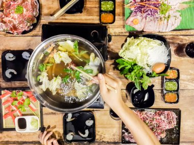 Sukiyaki ve shabu çorbası yerken el ele tutuşmak köfte, beyaz lahana, yengeç, vermicelli, karides ve ahşap bir fincanda.