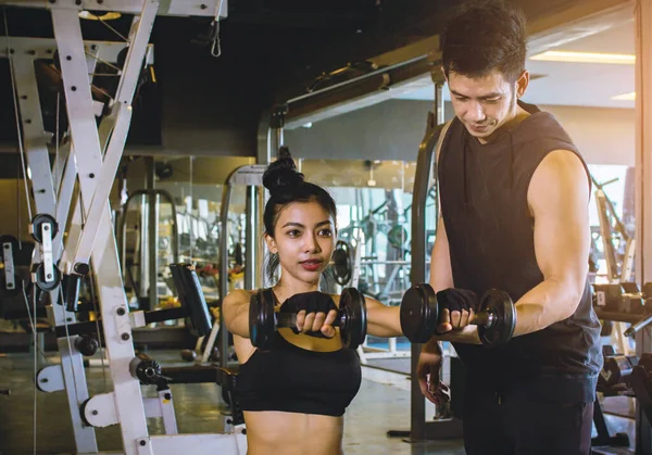 Asian people Sport girl doing weight exercises working with heavy dumbbells her personal trainer at Gym workout