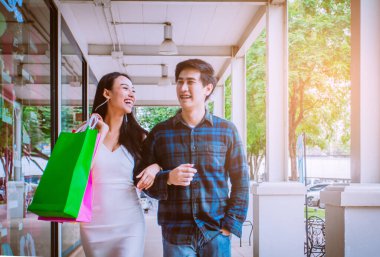 Beyaz ve siyah elbiseli genç bir Asyalı çift. Alışveriş torbaları sokak şehrinde eğleniyor. Alışveriş Konsepti