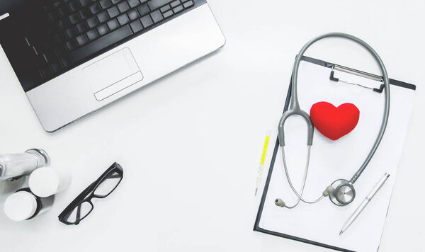 Вид сверху. Медицинские инструменты, технологический ноутбук, стетоскоп и очки на белом столе.