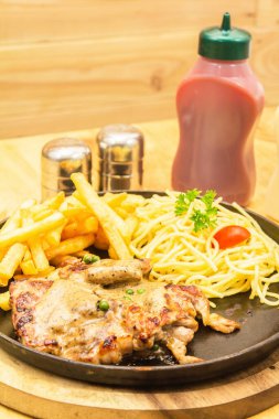 Domuz bifteği, patates kızartması ve ahşap bir masaya yerleştirilmiş spagetti..