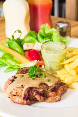 Domuz bifteği, patates kızartması ve salata, ahşap bir masaya konmuş..