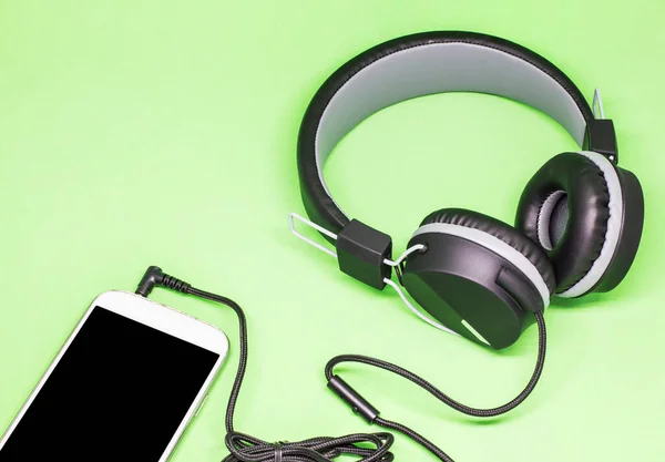 black headphones with the phone isolated on green background.