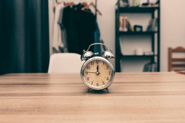retro stainless steel alarm clock on wooden table at the bedroom interior decor with bookshelf , and clothes at home