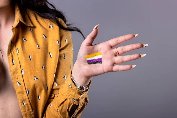 Young non-binary woman showing non-binary gender flag in hand. Close-up.