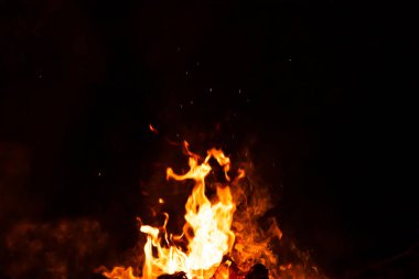 Yanan kırmızı kıvılcımlar gecenin büyük ateşinden yükselir. Yangın arka planda kıvılcım saçar. Soyut koyu parıltılı ateş parçacıkları ışıkları.
