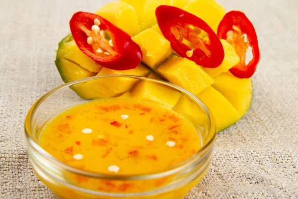 Close-up of diced half of mango, sliced red hot pepper and mango chili sauce on burlap. Rustic style. Soft focus