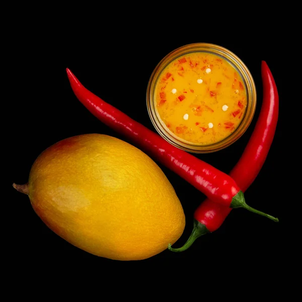 Mango chili sauce, ripe mango and two red hot peppers isolated on black