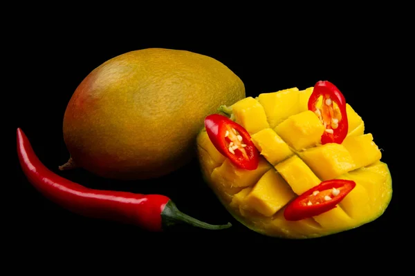 Whole mango, whole chili pepper, sliced hot pepper and cutted half of mango isolated on black background. Ingredients for Spicy mango chutney. Soft focus