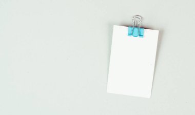 Gri arkaplanda ataç olan boş beyaz kağıt, metin için alanı kopyala, ofiste hatırlatma veya mesaj, iletişim konsepti