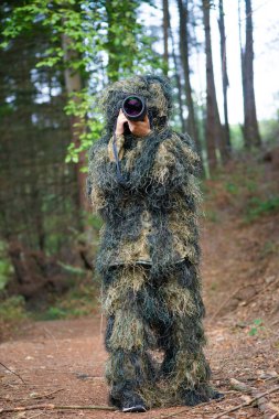 Ormanda kamuflaj kıyafeti giyen bir fotoğrafçı, kameralı vahşi yaşam fotoğrafçılığı ve telefoto lensleri.