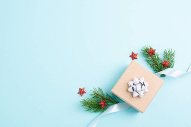 Noel tebrik kartı içinde küçük hediye kutusu, yıldızlar, kurdele ve köknar dalları, mavi arka plan 