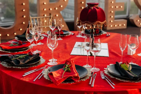 客人餐桌设置为黑色 红色和金色风格的宴会 精致的晚餐 餐巾纸盘 新鲜玫瑰 屋顶上的派对庆祝活动 — 图库照片