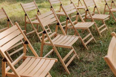 Parktaki çimlerin üzerinde duran misafirler için ahşap sandalyeler. Düğün töreni, açık hava etkinliği..